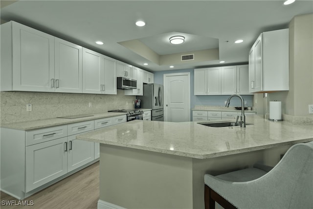 kitchen with white cabinets, sink, light stone countertops, kitchen peninsula, and stainless steel appliances