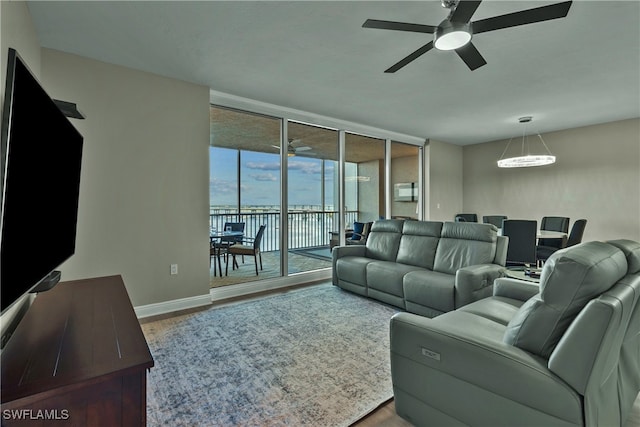 living room featuring hardwood / wood-style floors, a wall of windows, ceiling fan, and a water view