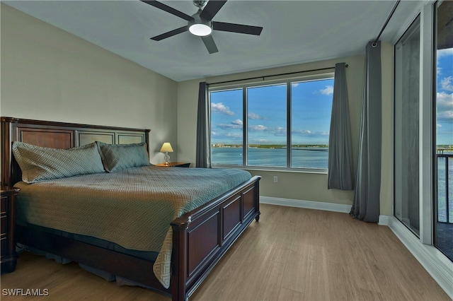 bedroom with light wood-type flooring, a water view, and ceiling fan