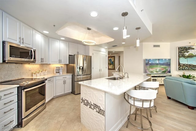 kitchen featuring stainless steel appliances, white cabinetry, sink, hanging light fixtures, and a kitchen island with sink