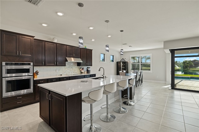 kitchen featuring decorative light fixtures, an island with sink, sink, a kitchen breakfast bar, and stainless steel double oven