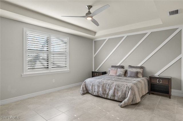 bedroom with ceiling fan, a tray ceiling, and light tile patterned floors