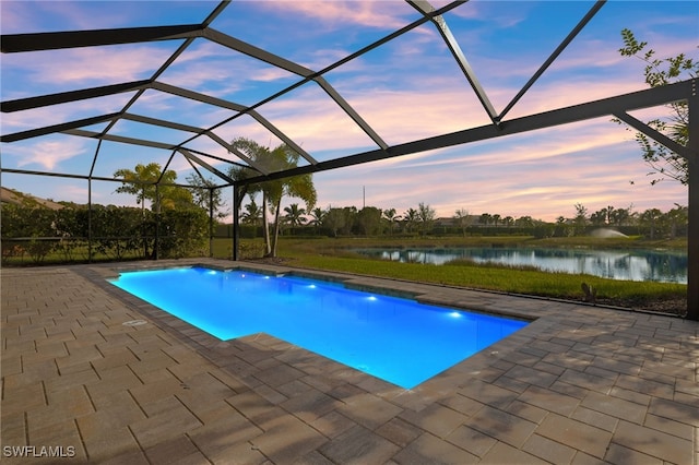 pool at dusk with a patio, a water view, and a lanai