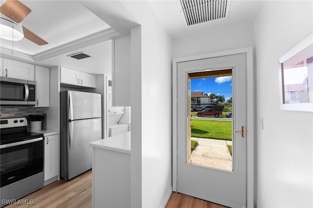 kitchen featuring stainless steel appliances, stacked washer and clothes dryer, a healthy amount of sunlight, and white cabinets