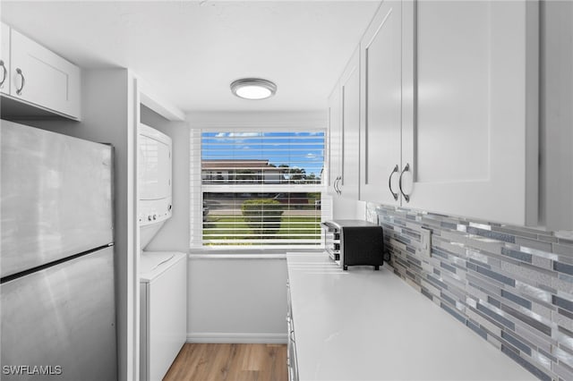 kitchen featuring light hardwood / wood-style floors, decorative backsplash, stainless steel refrigerator, white cabinetry, and stacked washer / drying machine