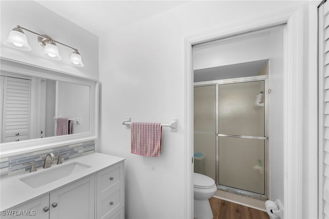 bathroom featuring walk in shower, hardwood / wood-style flooring, backsplash, vanity, and toilet