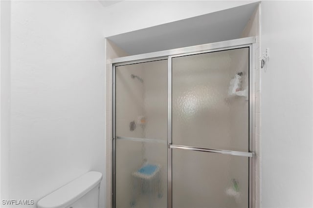 bathroom featuring a shower with shower door and toilet