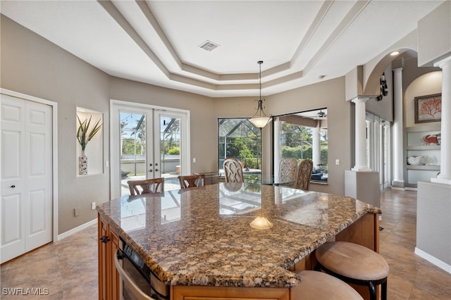 kitchen with ornate columns, pendant lighting, a kitchen island, and dark stone countertops