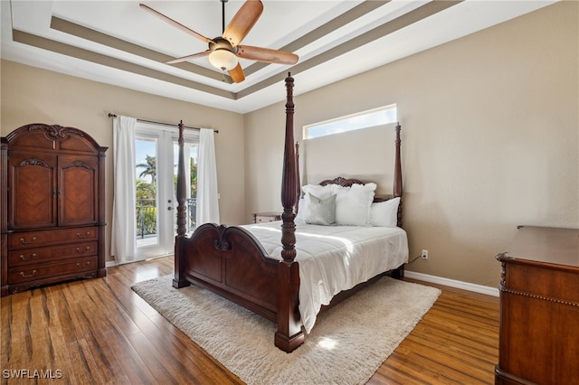 bedroom featuring access to outside, wood-type flooring, ceiling fan, and a tray ceiling