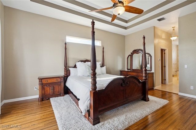 bedroom with connected bathroom, wood-type flooring, ceiling fan, and a raised ceiling