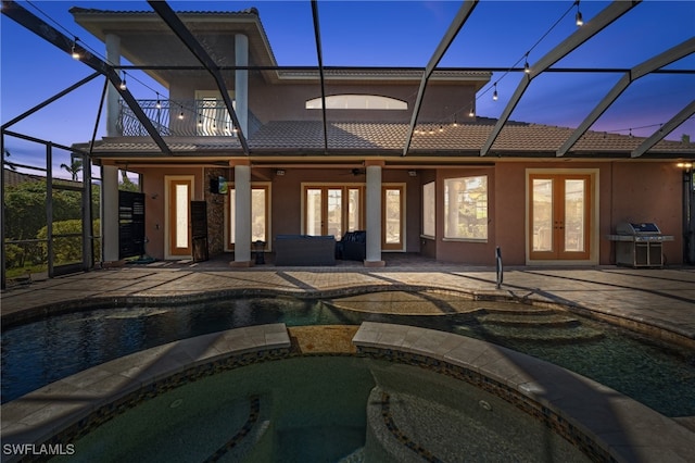 back house at dusk with a swimming pool with hot tub, a balcony, ceiling fan, a patio, and french doors