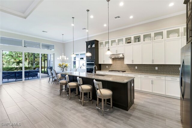 kitchen with sink, hanging light fixtures, appliances with stainless steel finishes, an island with sink, and light stone countertops