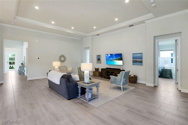 living room featuring visible vents, baseboards, a raised ceiling, light wood-style flooring, and crown molding