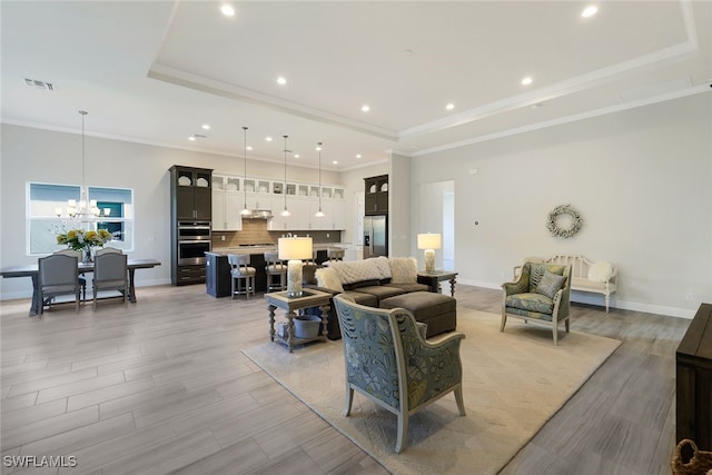 living room with a notable chandelier, ornamental molding, a raised ceiling, and light wood-type flooring