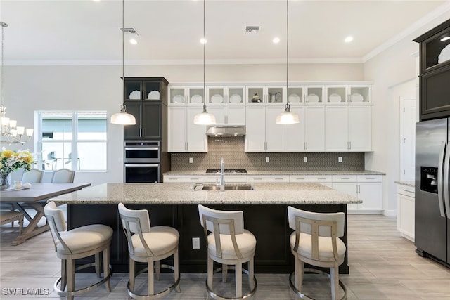 kitchen featuring appliances with stainless steel finishes, hanging light fixtures, ornamental molding, light stone counters, and a center island with sink