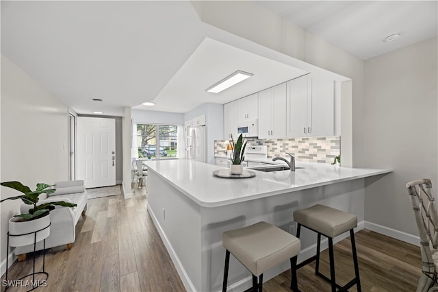 kitchen with white cabinets, decorative backsplash, kitchen peninsula, light wood-type flooring, and white appliances