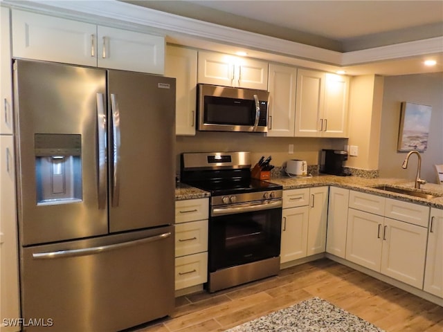 kitchen with appliances with stainless steel finishes, sink, light hardwood / wood-style floors, and white cabinets