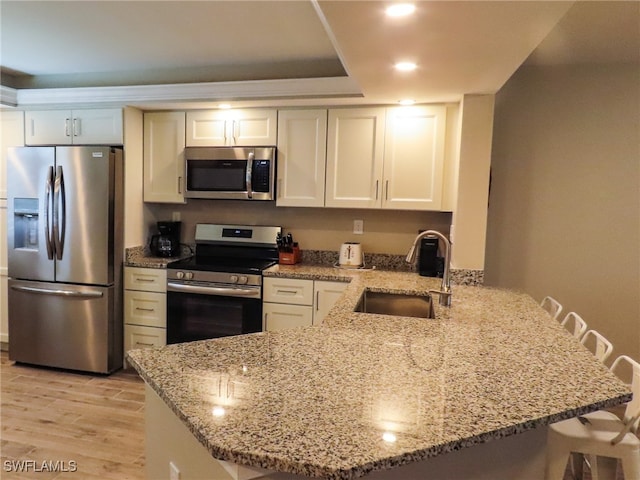 kitchen featuring stainless steel appliances, kitchen peninsula, sink, light stone countertops, and light hardwood / wood-style flooring