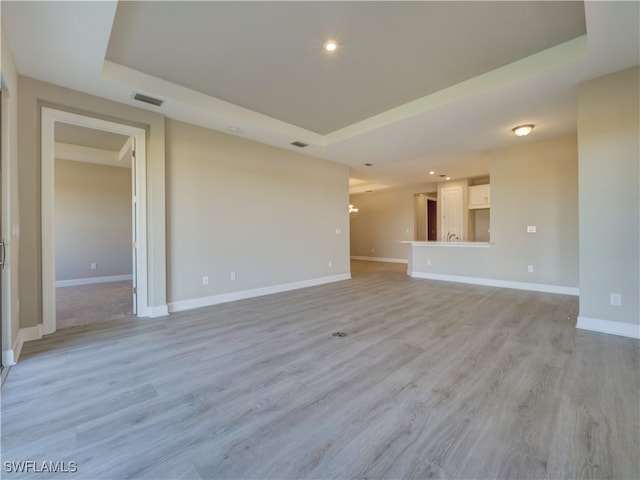 unfurnished living room featuring a raised ceiling and light wood-type flooring