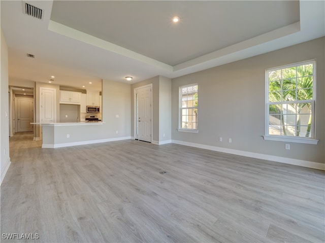 unfurnished living room with a raised ceiling and light hardwood / wood-style floors