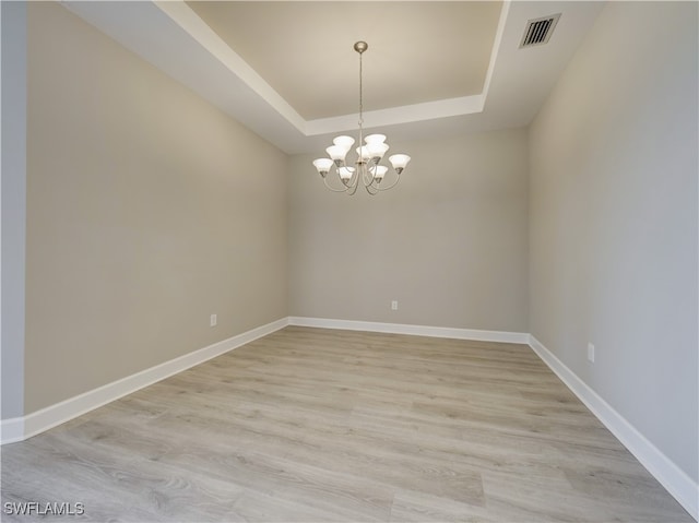 spare room with an inviting chandelier, a raised ceiling, and light hardwood / wood-style flooring