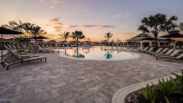 pool at dusk with a water view and a patio area