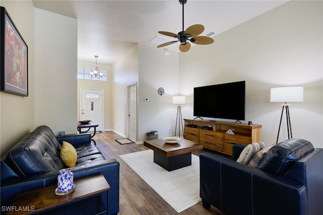 living room featuring dark wood-type flooring, ceiling fan with notable chandelier, and a high ceiling