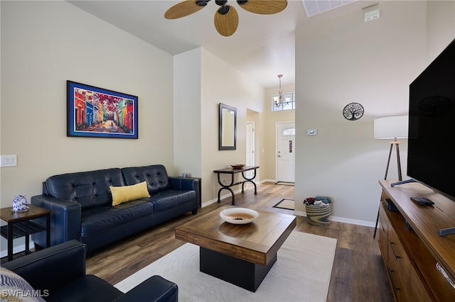 living room featuring dark hardwood / wood-style flooring, ceiling fan with notable chandelier, and a towering ceiling