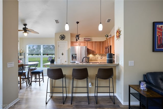 kitchen featuring hanging light fixtures, ceiling fan, stainless steel appliances, light stone countertops, and backsplash