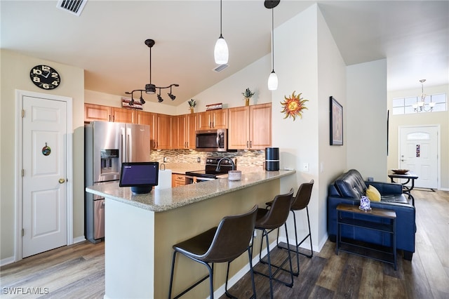 kitchen with appliances with stainless steel finishes, pendant lighting, kitchen peninsula, and decorative backsplash