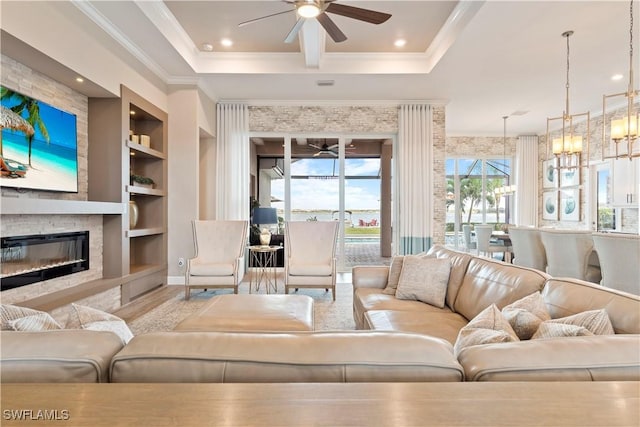 living room with a tray ceiling, built in shelves, ceiling fan with notable chandelier, and ornamental molding