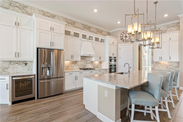 kitchen featuring premium range hood, sink, beverage cooler, a kitchen island with sink, and stainless steel appliances