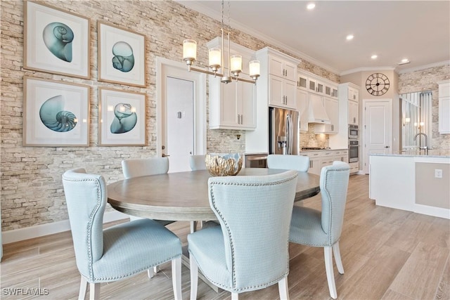 dining space with crown molding, sink, an inviting chandelier, and light hardwood / wood-style flooring