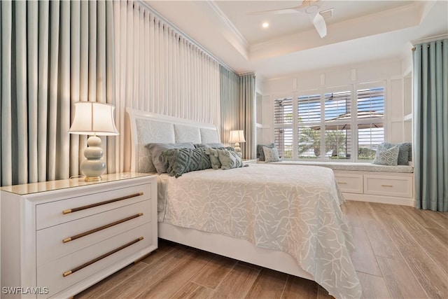 bedroom featuring a raised ceiling, ornamental molding, and light wood-type flooring