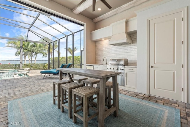 view of patio with sink, glass enclosure, a water view, a grill, and area for grilling