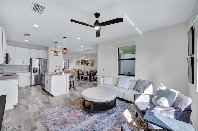 living room featuring light wood-type flooring, ceiling fan, and sink