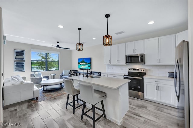 kitchen featuring a kitchen island with sink, white cabinets, hanging light fixtures, sink, and appliances with stainless steel finishes