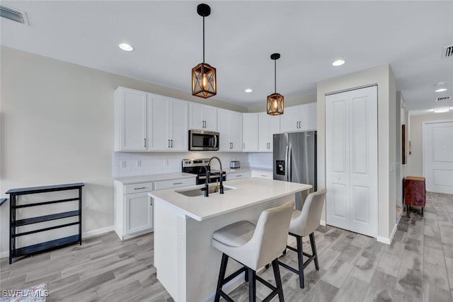 kitchen featuring appliances with stainless steel finishes, sink, decorative light fixtures, white cabinetry, and an island with sink