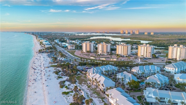 aerial view at dusk featuring a water view and a beach view