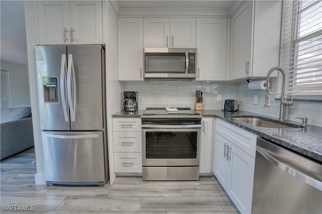 kitchen with sink, tasteful backsplash, dark stone counters, white cabinets, and appliances with stainless steel finishes