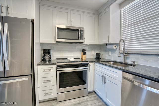 kitchen with white cabinets, appliances with stainless steel finishes, sink, and dark stone counters