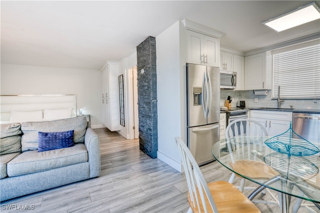 kitchen featuring decorative backsplash, stainless steel appliances, sink, light hardwood / wood-style floors, and white cabinetry