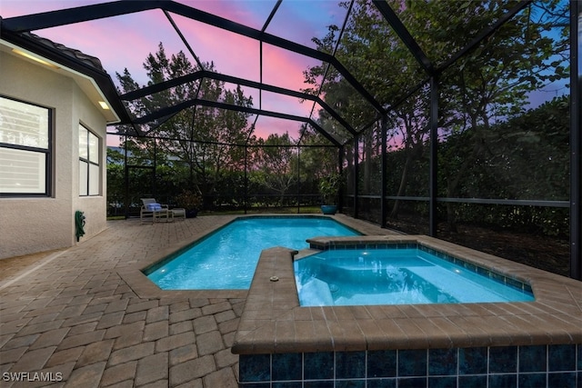 pool at dusk featuring a lanai, a patio area, and an in ground hot tub