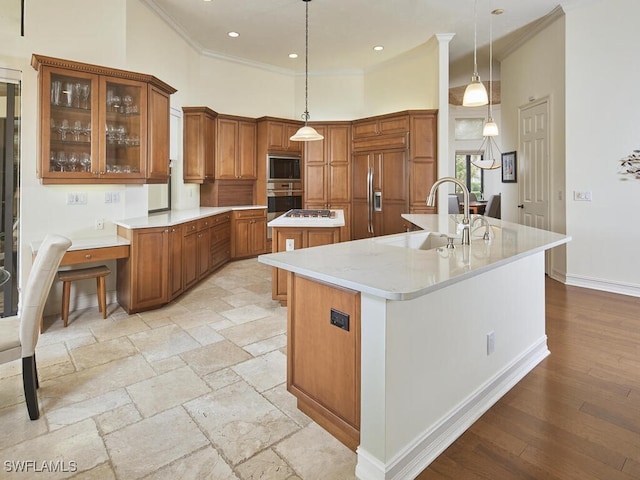 kitchen with a high ceiling, decorative light fixtures, built in appliances, sink, and a kitchen island with sink