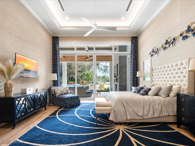 bedroom featuring access to exterior, a tray ceiling, ornamental molding, and wood finished floors