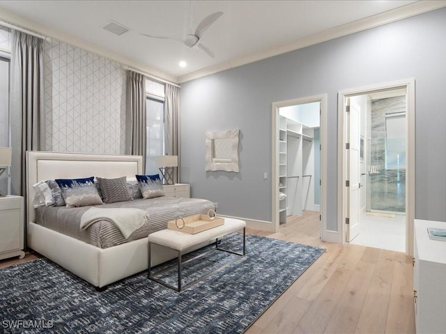 bedroom with a walk in closet, an accent wall, ornamental molding, wood finished floors, and baseboards