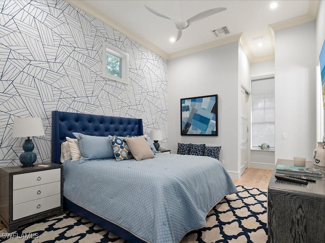 bedroom featuring crown molding, visible vents, an accent wall, light wood-style floors, and baseboards