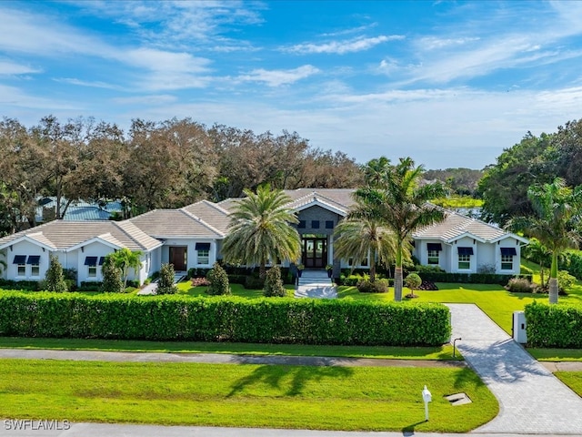 view of front of home with decorative driveway, a front yard, french doors, and a tile roof