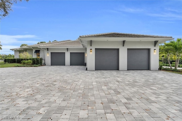 view of front of home with an attached garage, a tile roof, decorative driveway, and stucco siding