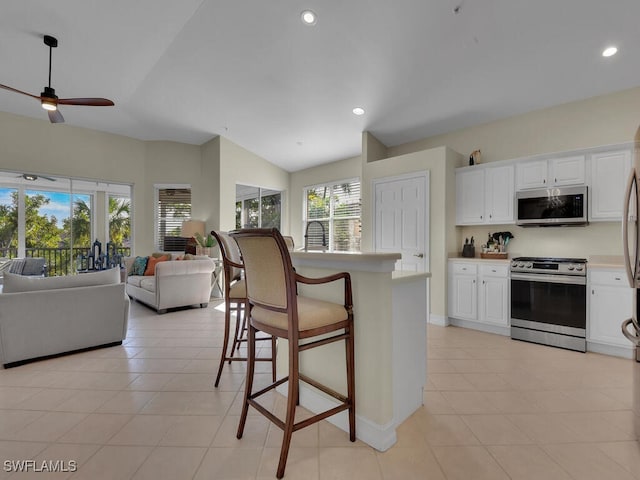 kitchen with stainless steel appliances, vaulted ceiling, ceiling fan, a breakfast bar, and white cabinetry